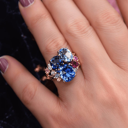 Close-up of a gold sapphire ring with blue and pink sapphires and diamonds on dark velvet, highlighting the gems' brilliance and intricate craftsmanship.