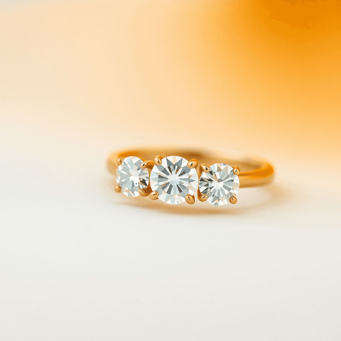 Close-up of a three-stone diamond ring with sparkling diamonds on a classic gold band against a soft, warm neutral background.