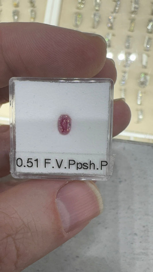Small pink gemstone in a clear case held by a hand, with '0.51 F.V. Posh P' text.