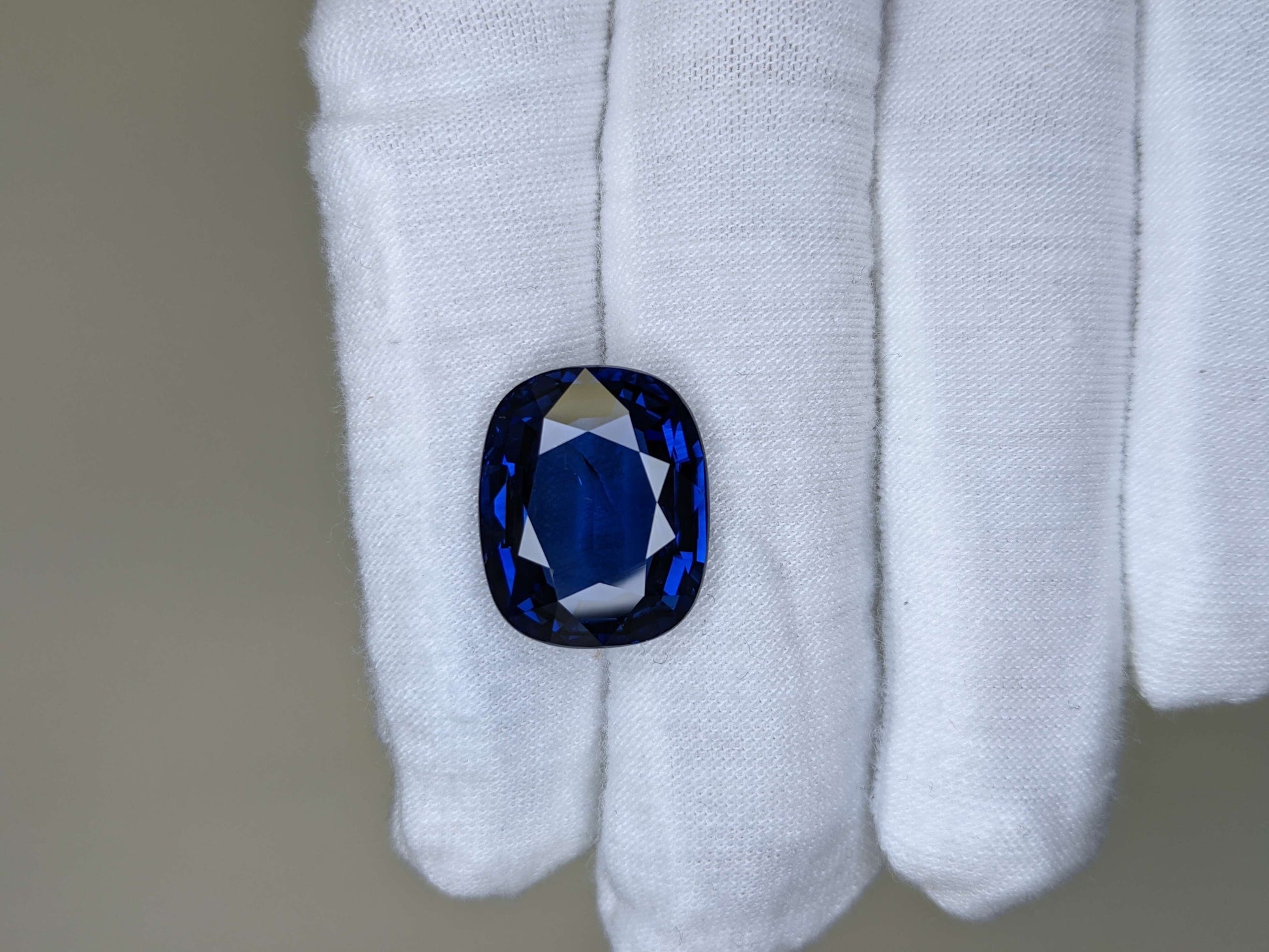 Blue gemstone held in a white glove against a neutral background