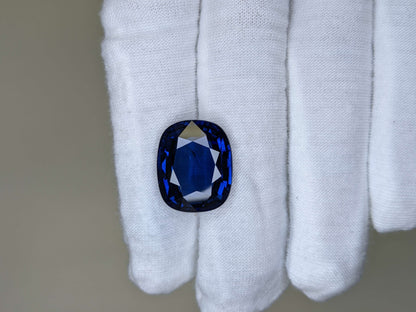 Blue gemstone held in a white glove against a neutral background