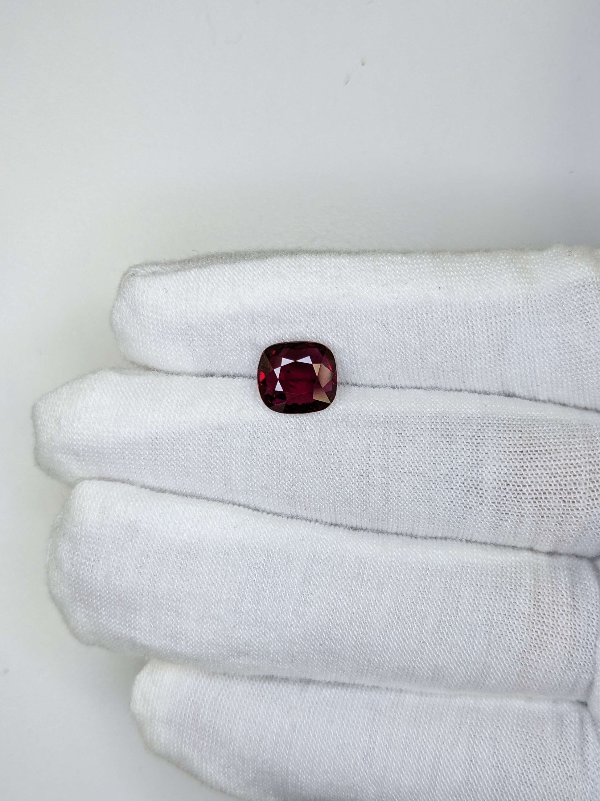 Red gemstone held in a white glove against a light background