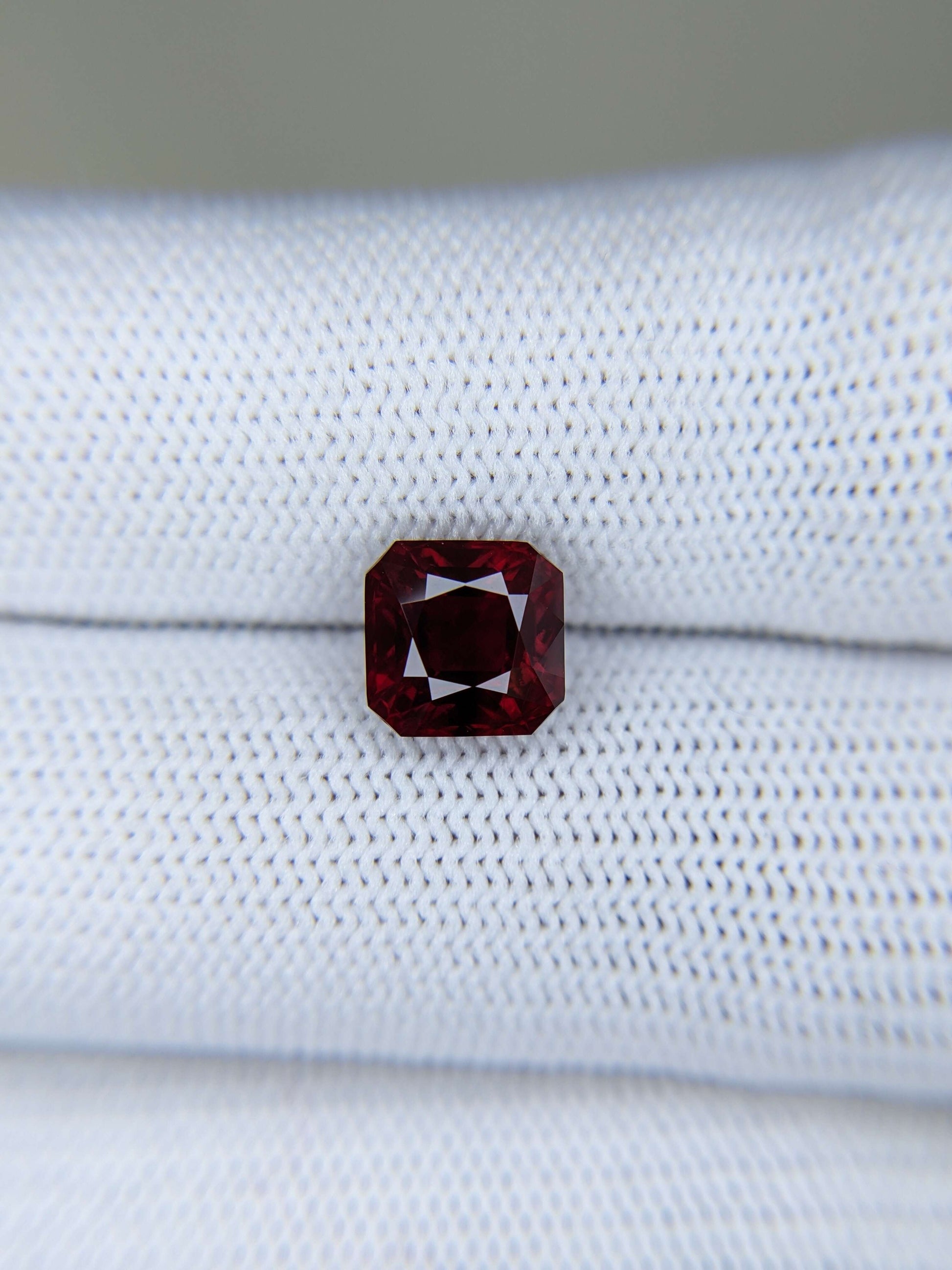 Emerald-cut red gemstone on a white fabric background