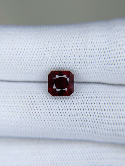 Emerald-cut red gemstone on a white fabric background