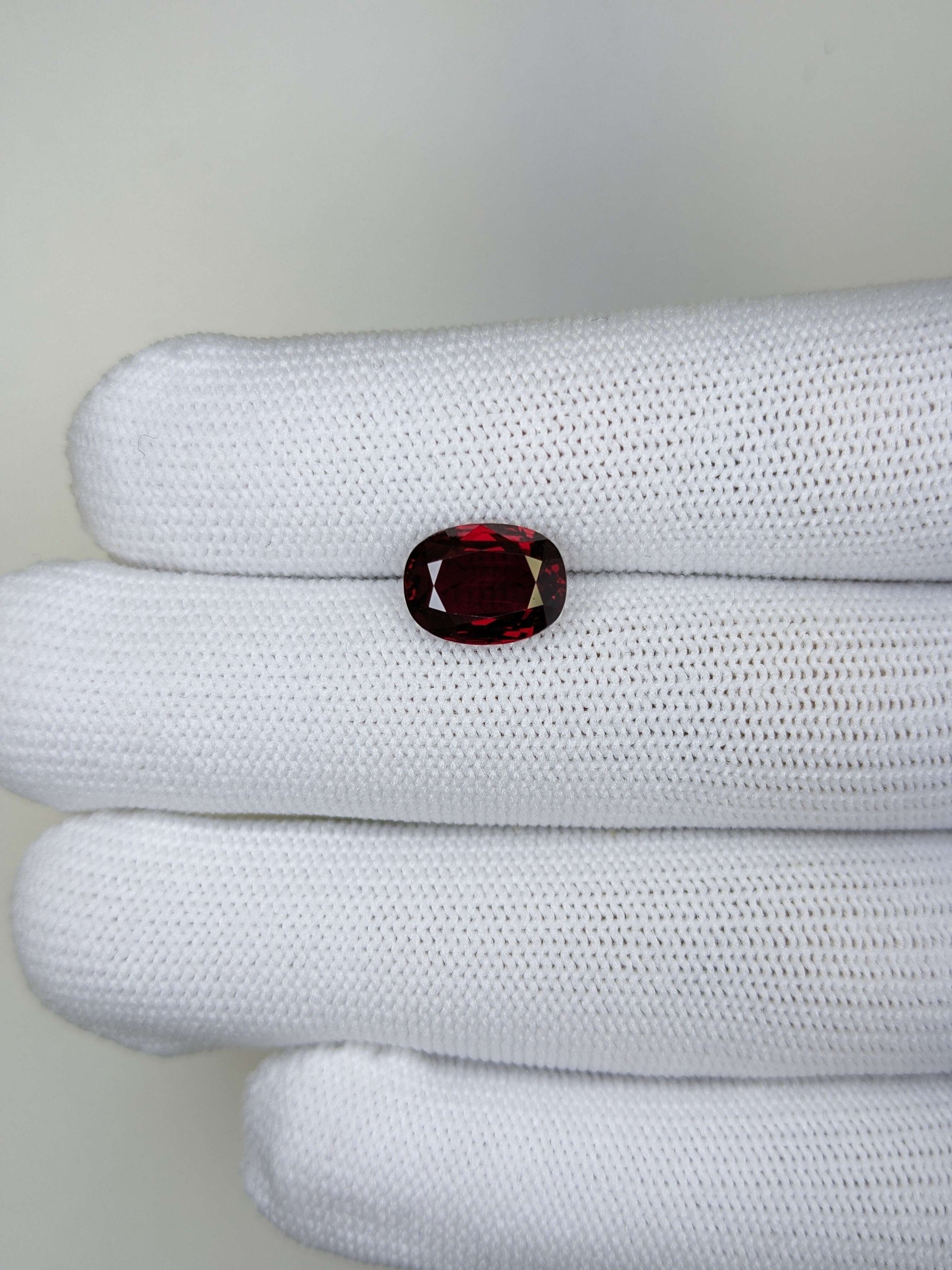 Ruby gemstone held between white gloves on a light gray background