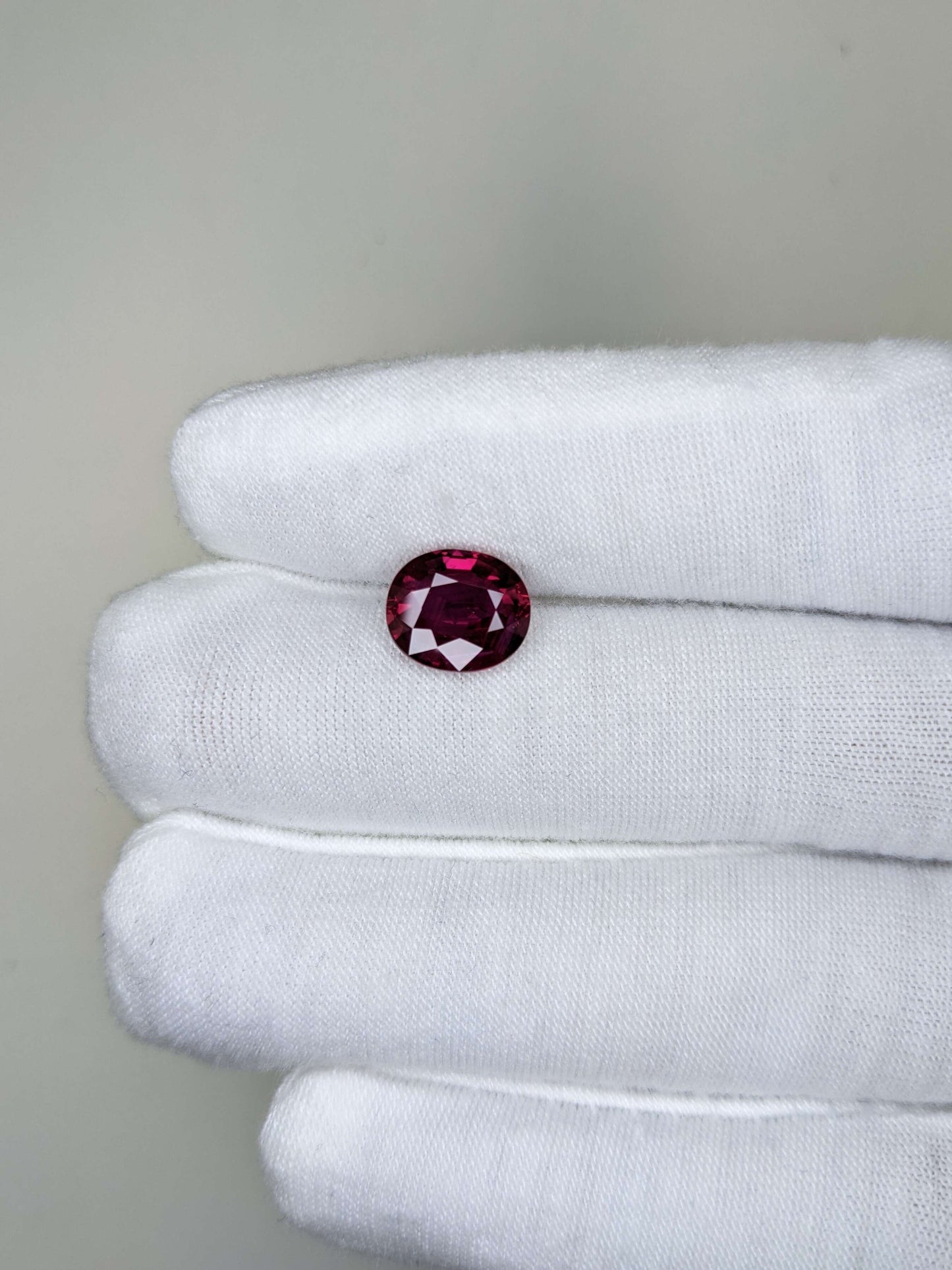 Red Ruby no heat gemstone held between white gloves on a neutral background
