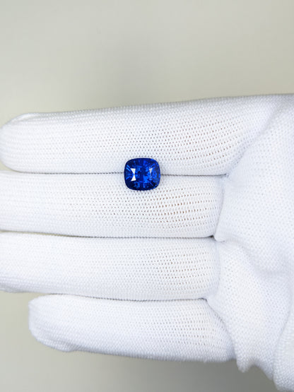Blue gemstone held in a white glove against a neutral background