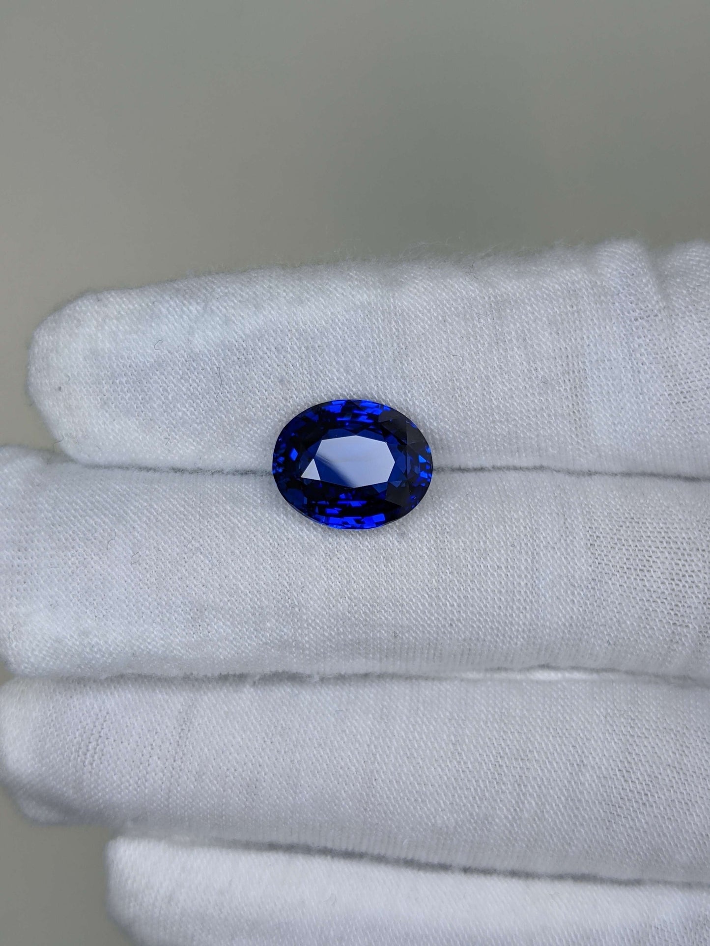 Blue gemstone held between white gloves on a neutral background