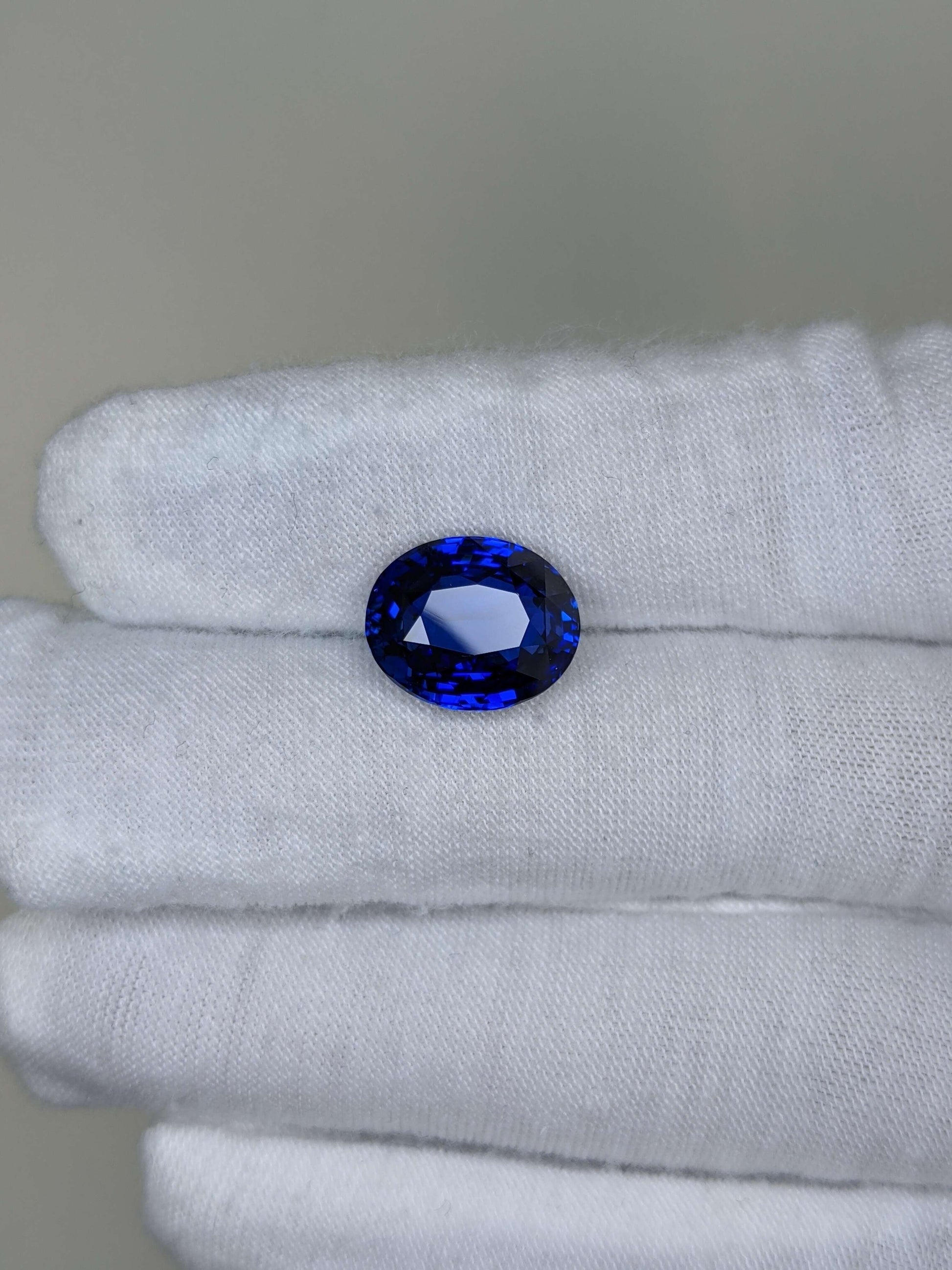 Blue gemstone held between white gloves on a neutral background