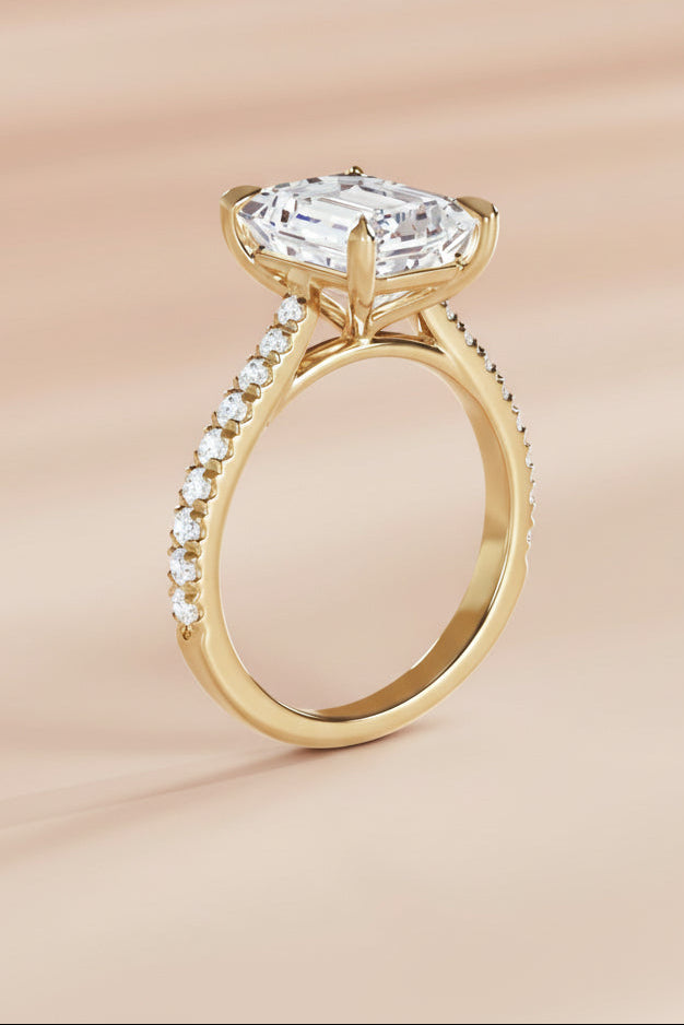 Gold ring with a large diamond and smaller diamonds on the band against a beige background