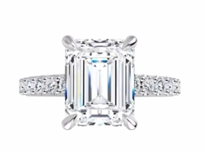 Diamond ring with emerald-cut center stone on a white background