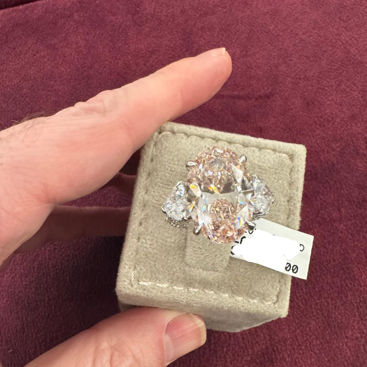 Diamond ring in a box held by a hand on a maroon background