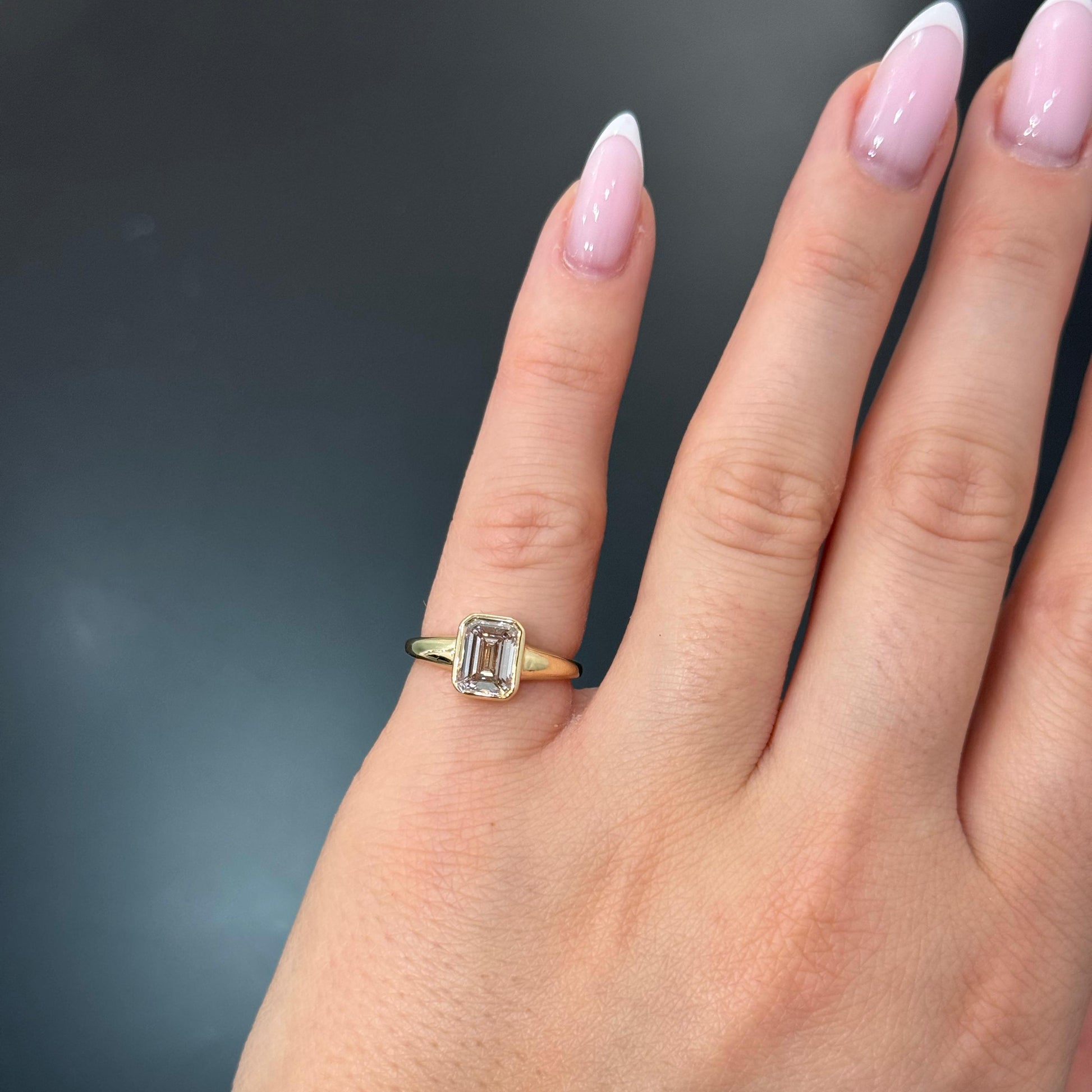 Liora-Jade 1.37 Carat Emerald Cut Lab Grown Diamond Solitaire Bezel Engagement Ring in 14k Yellow Gold On Hand