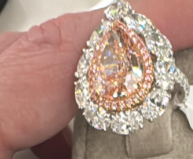 Teardrop-shaped diamond ring with rose gold accents on a display stand, featuring a price tag.