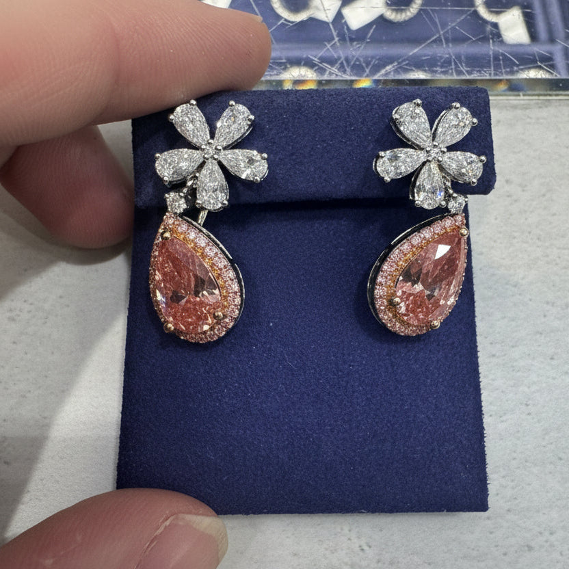 Diamond earrings on a blue display, held by a hand.