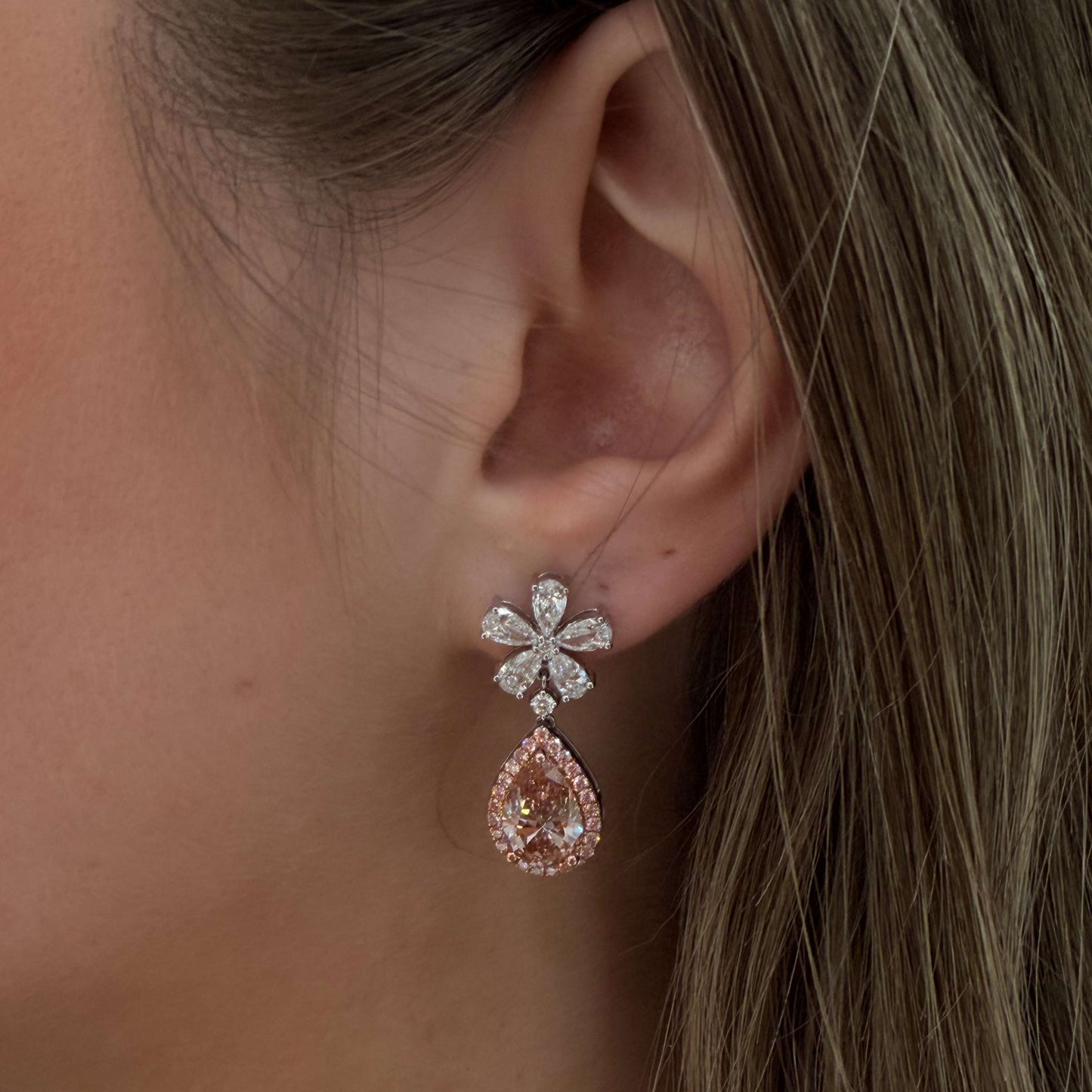 Close-up of a woman's ear wearing a floral earring with a pink teardrop gemstone.