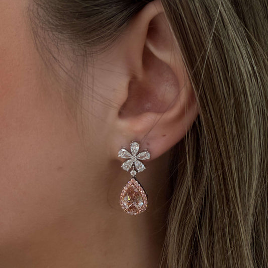 Close-up of a woman's ear wearing a floral earring with a pink teardrop gemstone.