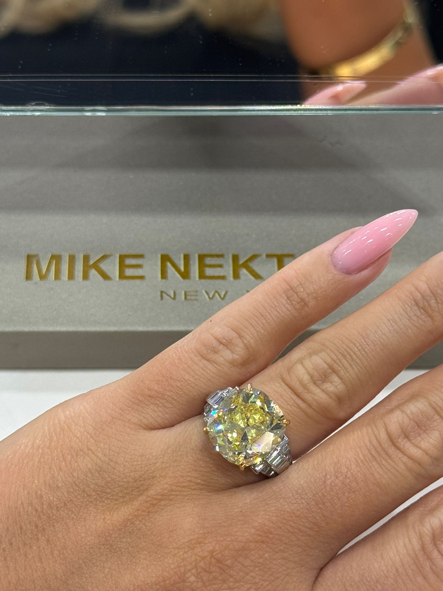 Hand wearing a large diamond ring with 'MIKE NEKTA New York' box in the background