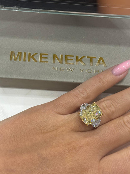Gold ring with a large gemstone on a hand, with 'MIKE NEKTA NEW YORK' brand box in the background.
