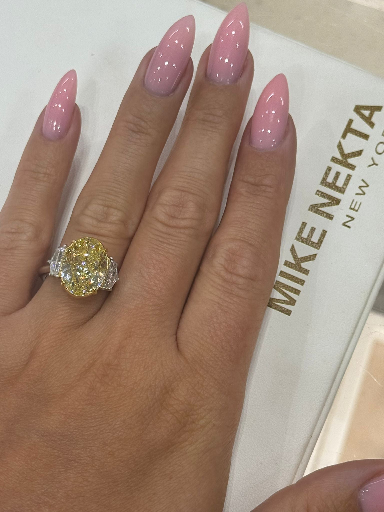 Hand wearing a large diamond ring with pink nail polish on a white background