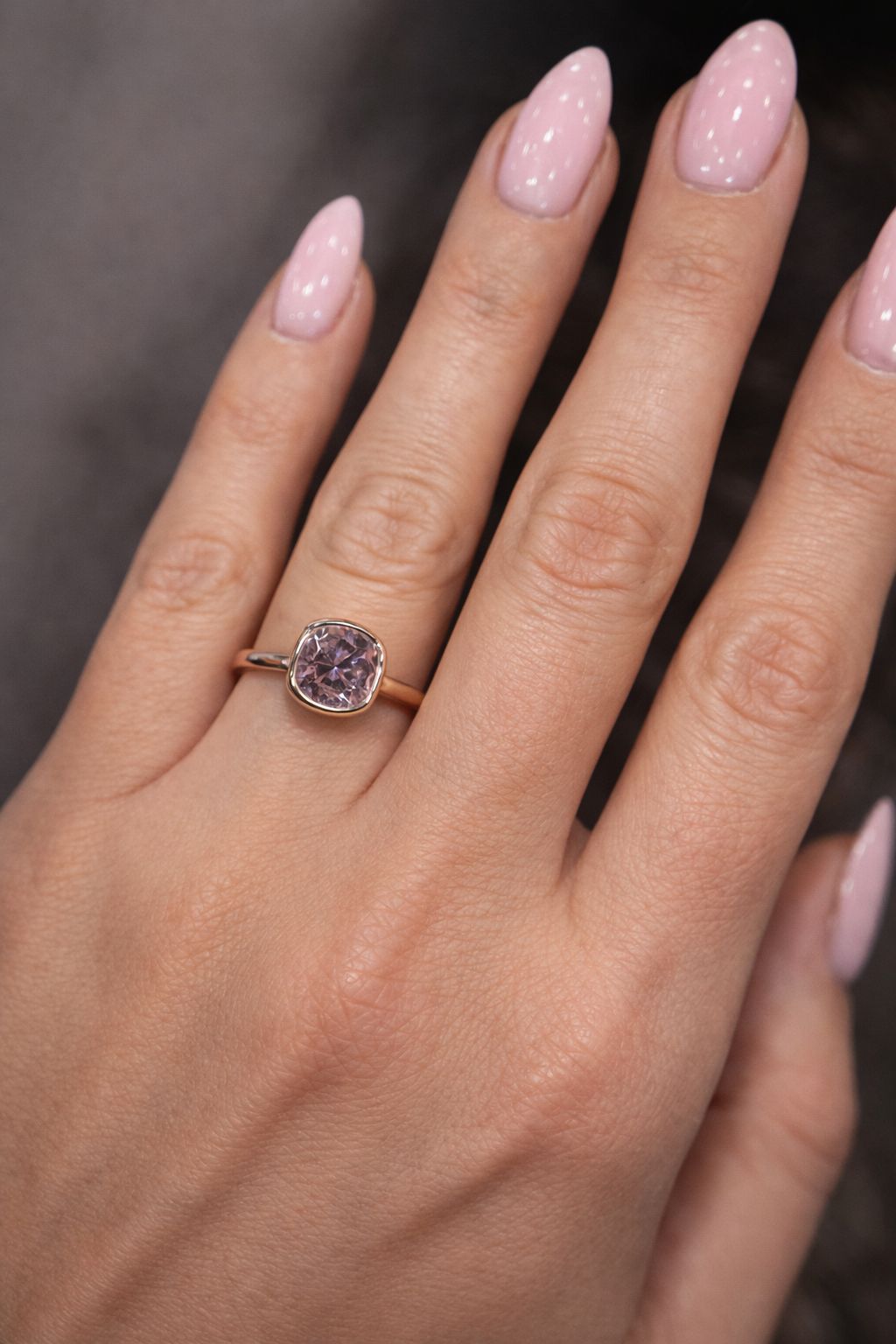 Hand wearing a rose gold ring with a pink diamond against a blurred background