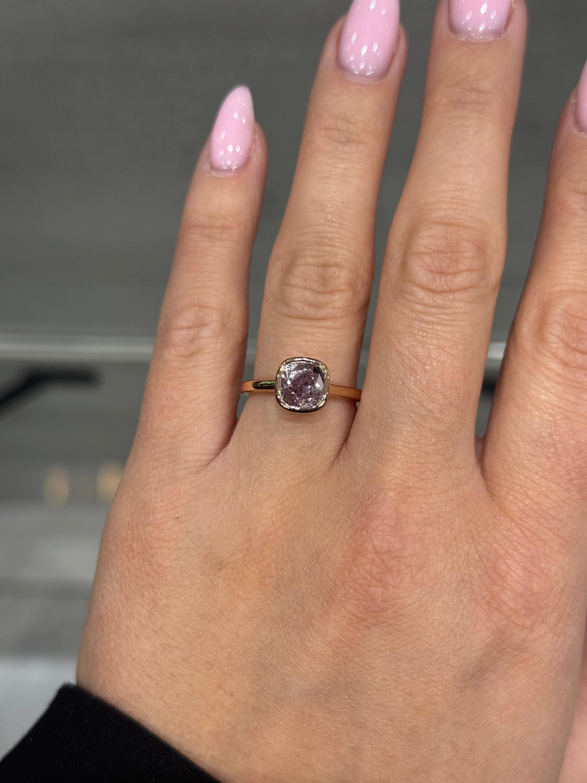 Hand wearing a ring with a pink diamond against a blurred background