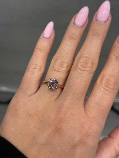 Hand wearing a ring with a pink diamond against a neutral background