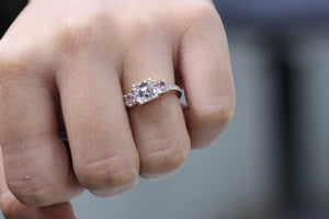 Three stone ring containing white, Asher cut diamond in the center and to Pink Diamond on the sides on a woman's finger